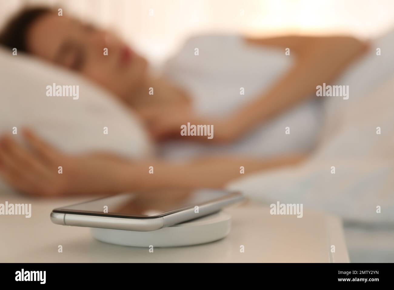 Smartphone charging on wireless pad and woman sleeping in bed Stock