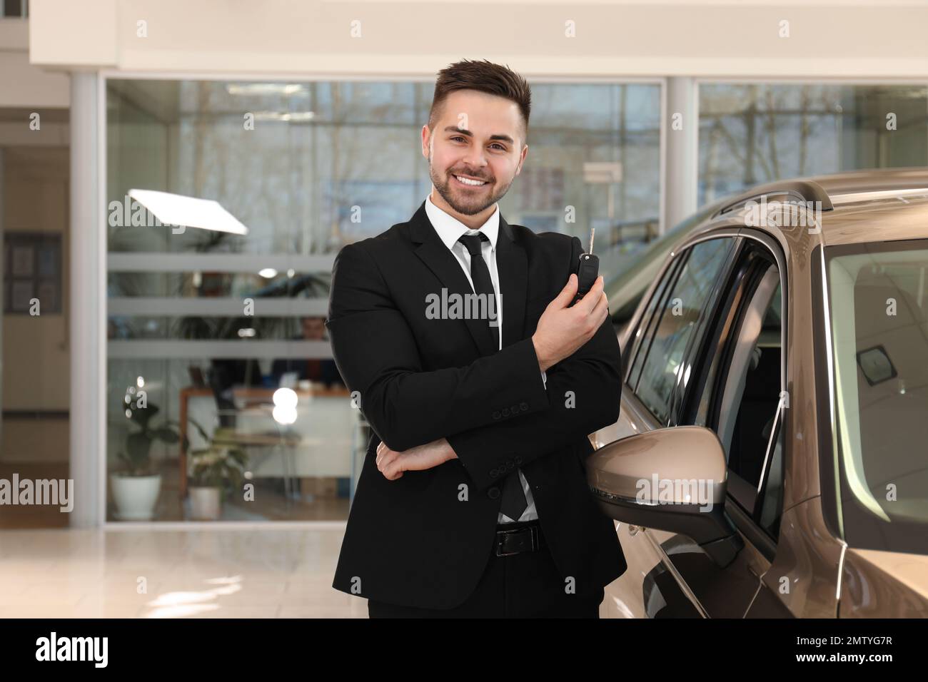 Young salesman with key near car in dealership Stock Photo - Alamy