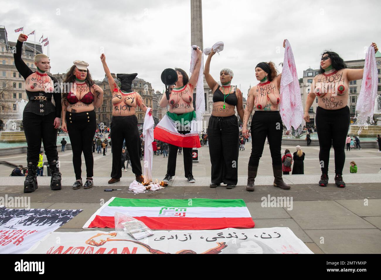 London, England, UK 01/02/2023 Women bare their breasts and bodies for a global Body Riot for Women Life Freedom on No Hijab Day. Women stood on the steps at Trafalgar Square with slogans on their body and symbolically burnt hijabs Stock Photo
