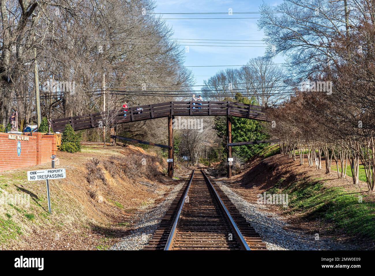 WAXHAW, NC, USA-28 JAN 2023: View down train tracks toward foot bridge, with people pausing on bridge.  Greenery. Stock Photo