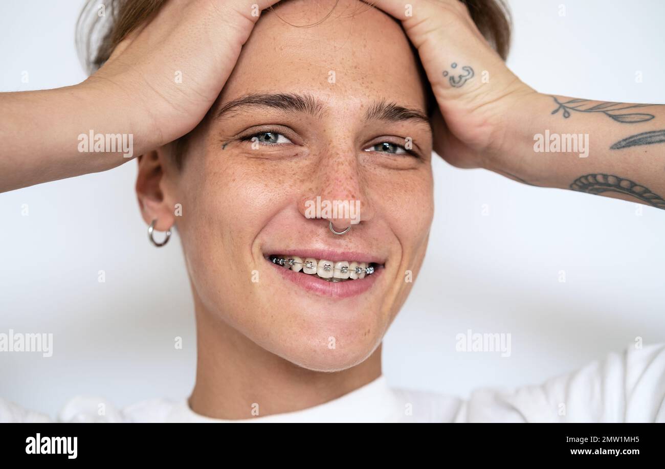 Female face close-up. Young woman with tattoos, facial piercing, braces on  teeth holding head in her hands and smiling looking at camera Stock Photo -  Alamy