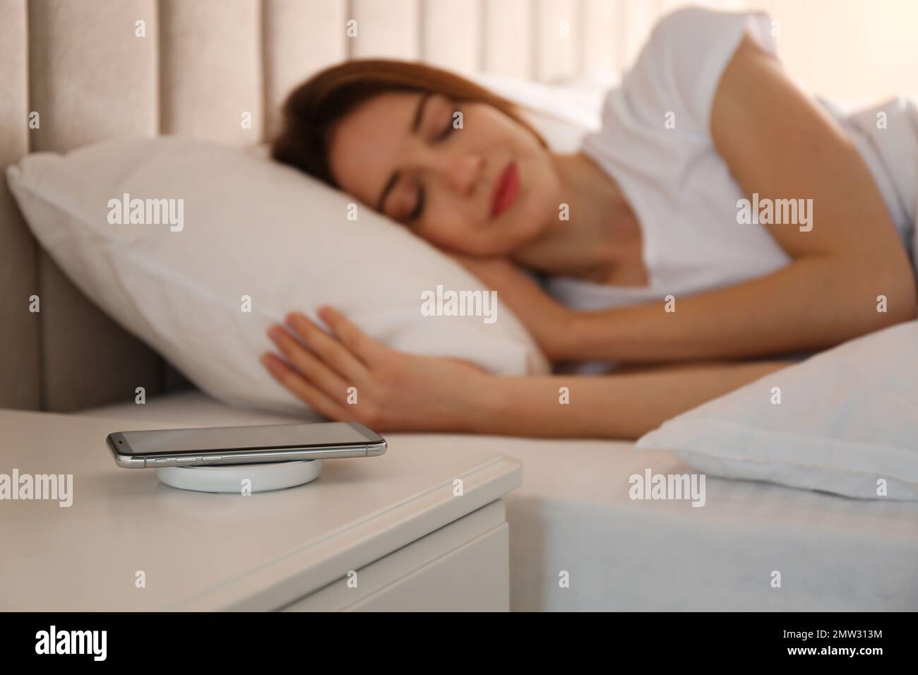 Smartphone charging on wireless pad and woman sleeping in bed Stock