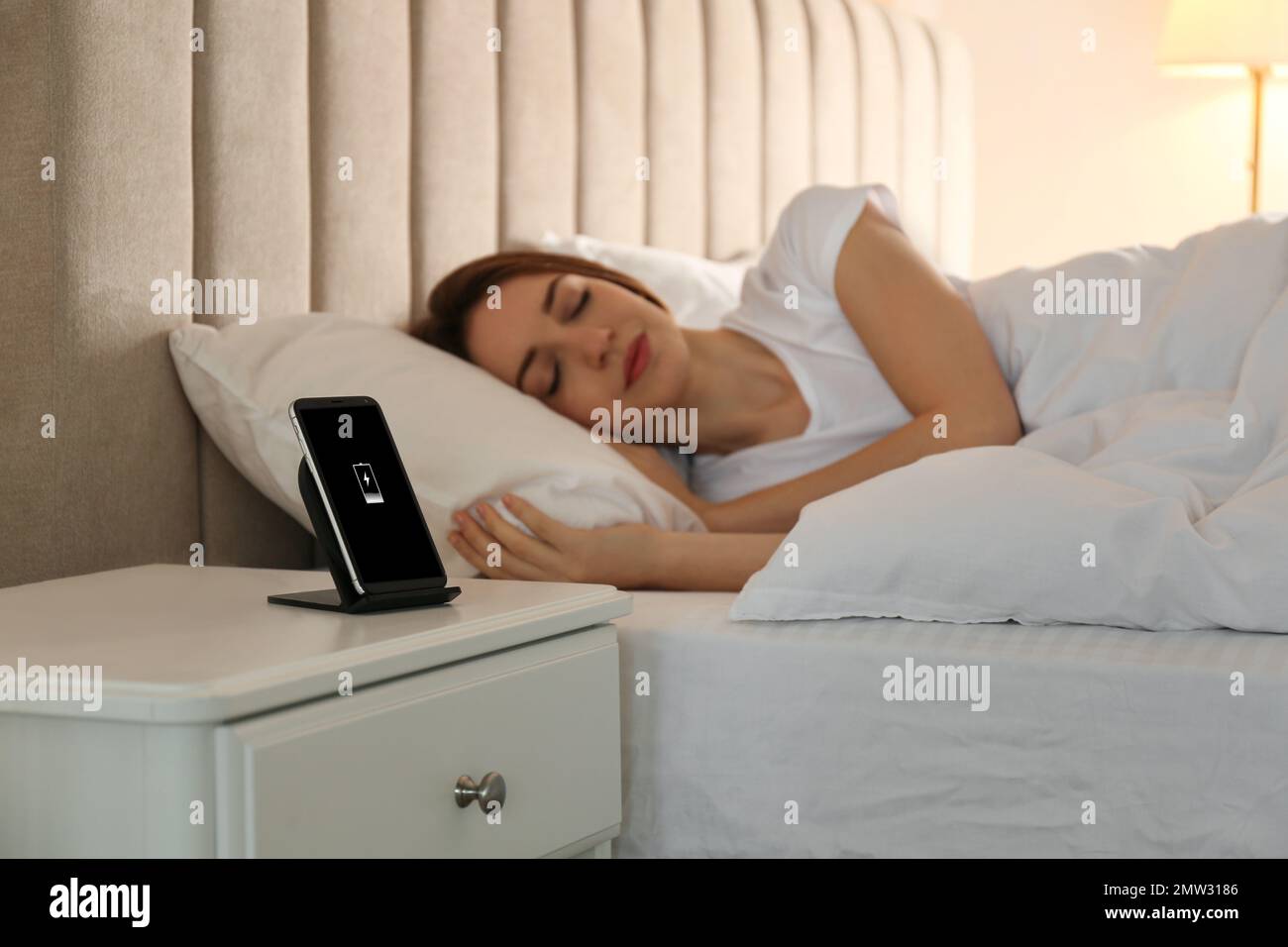 Smartphone charging on wireless pad and woman sleeping in bed Stock
