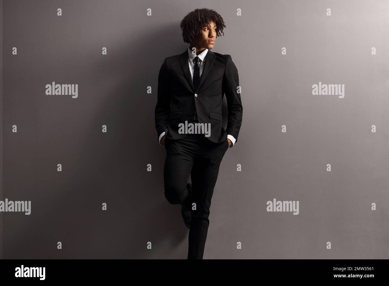 African american young man in a suit and tie leaning on a grey wall ...