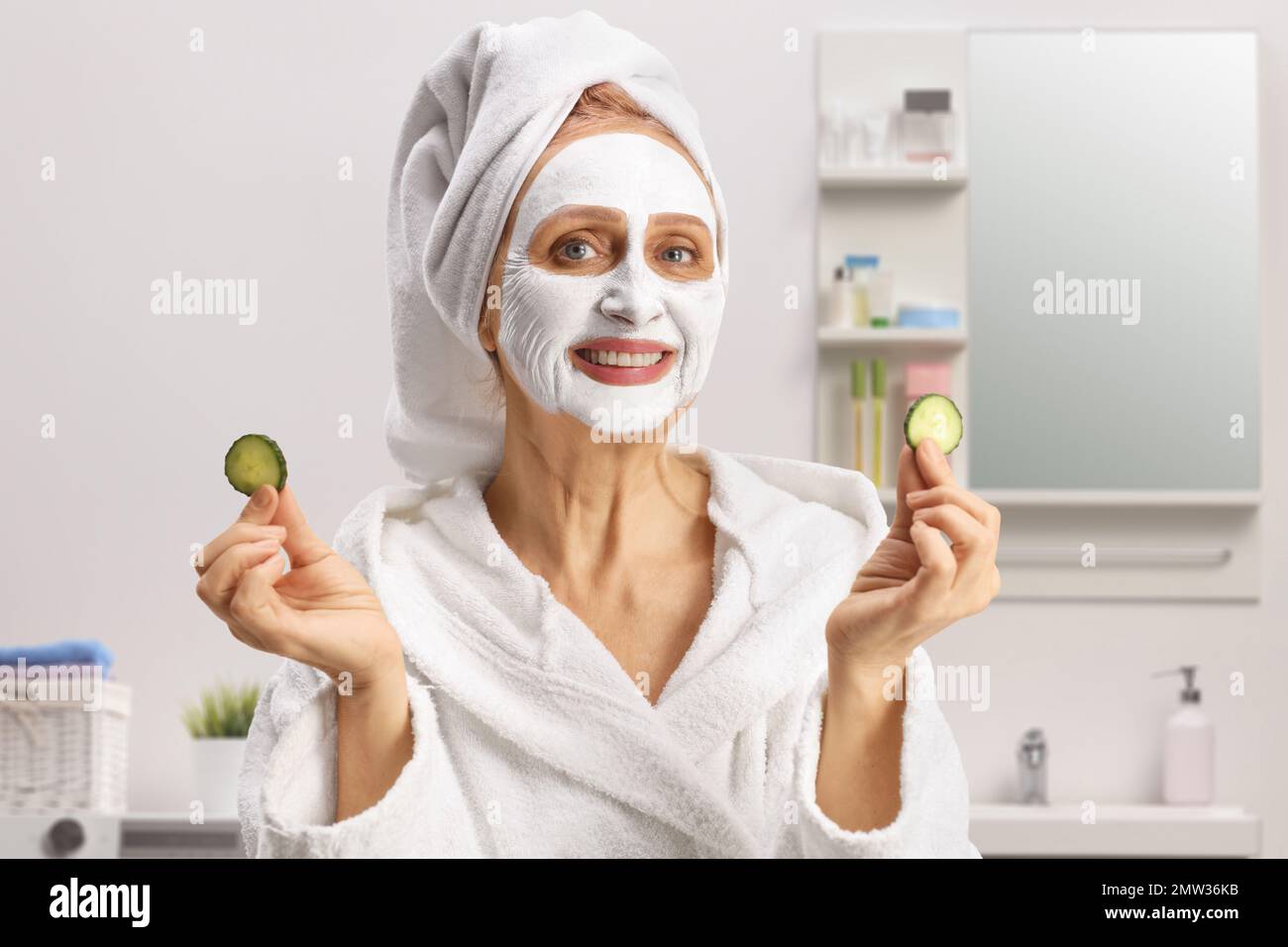 Beautiful woman with towel on her head and a face mask holding pieces of cucumber inside a