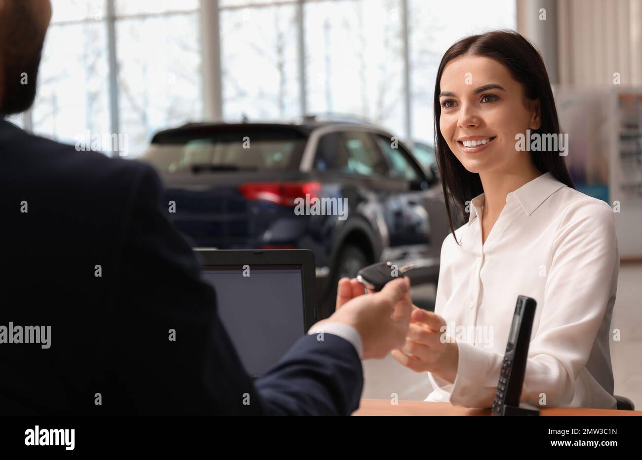 Salesman giving key to client in car dealership Stock Photo - Alamy