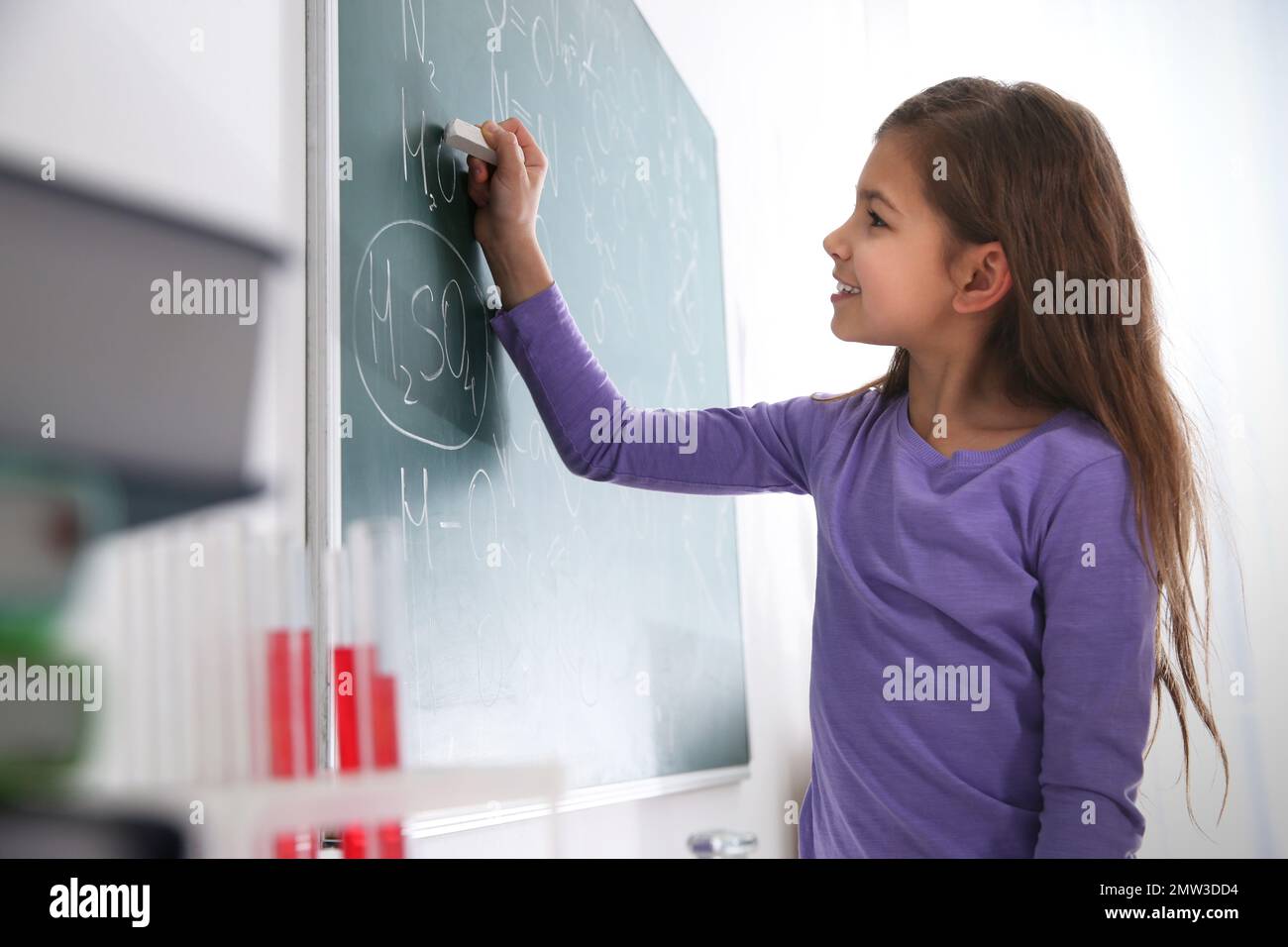 Schoolgirl writing chemical formulas on chalkboard in classroom Stock