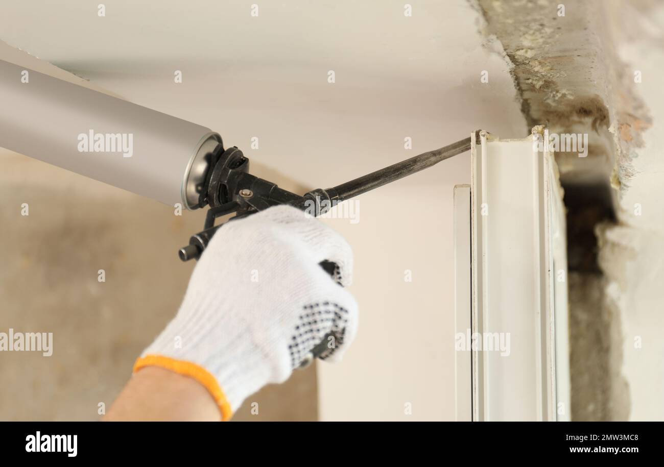 Worker using foam gun for window installation indoors, closeup Stock