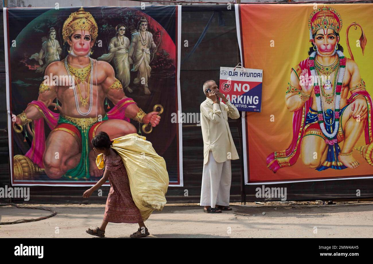 An Indian rag picker girl walks past pictures of Hindu monkey god ...