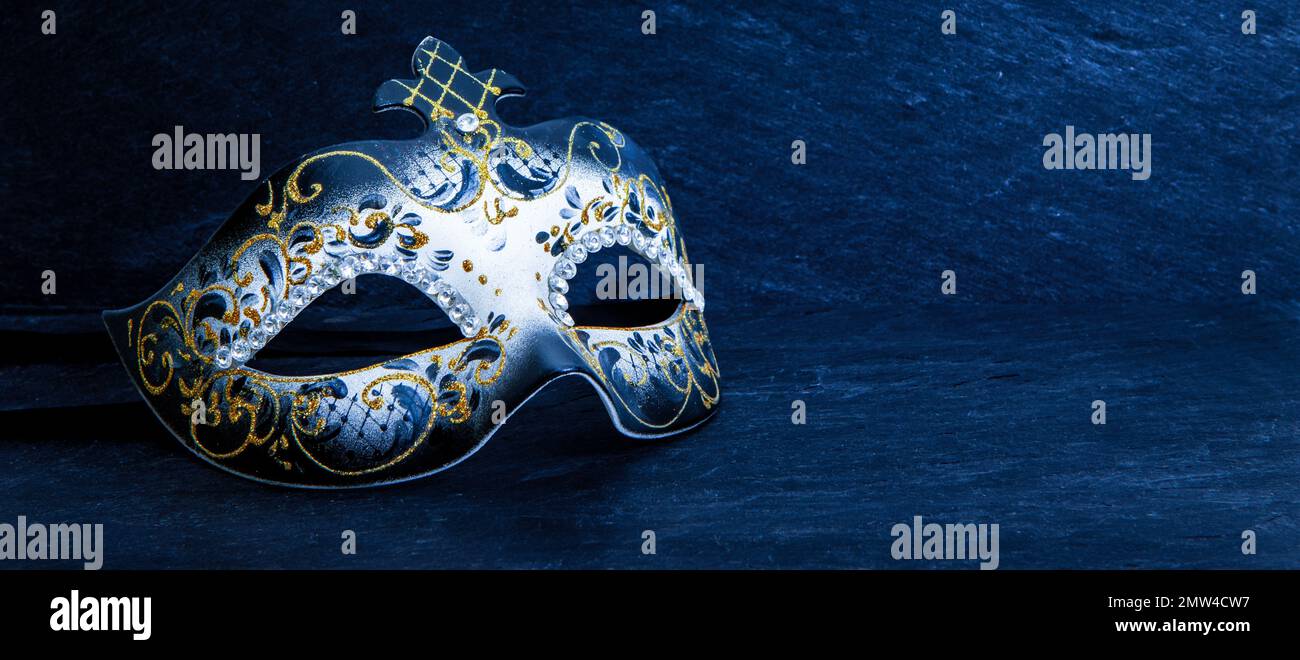 Festive Venetian carnival mask with gold glitter decorations and diamond beads on dark blue background. Stock Photo