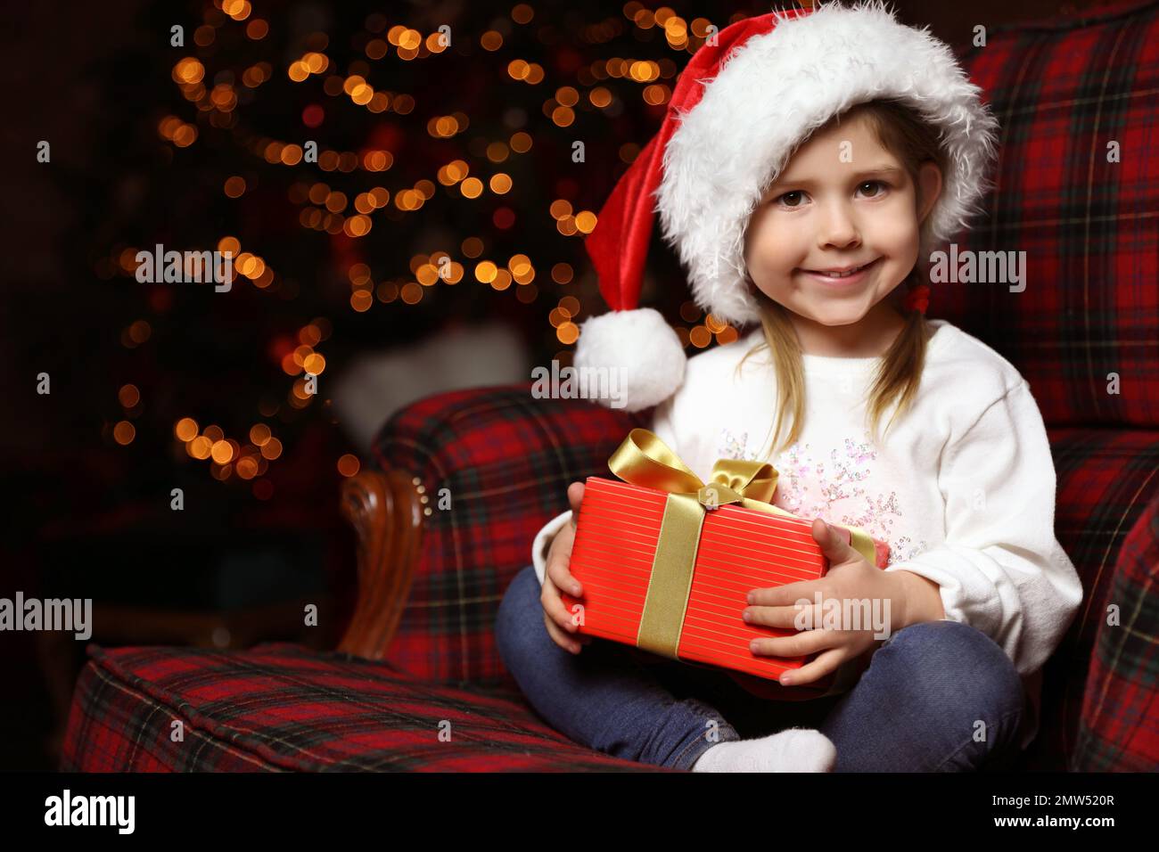 Cute little child with Christmas gift sitting in armchair at home Stock Photo