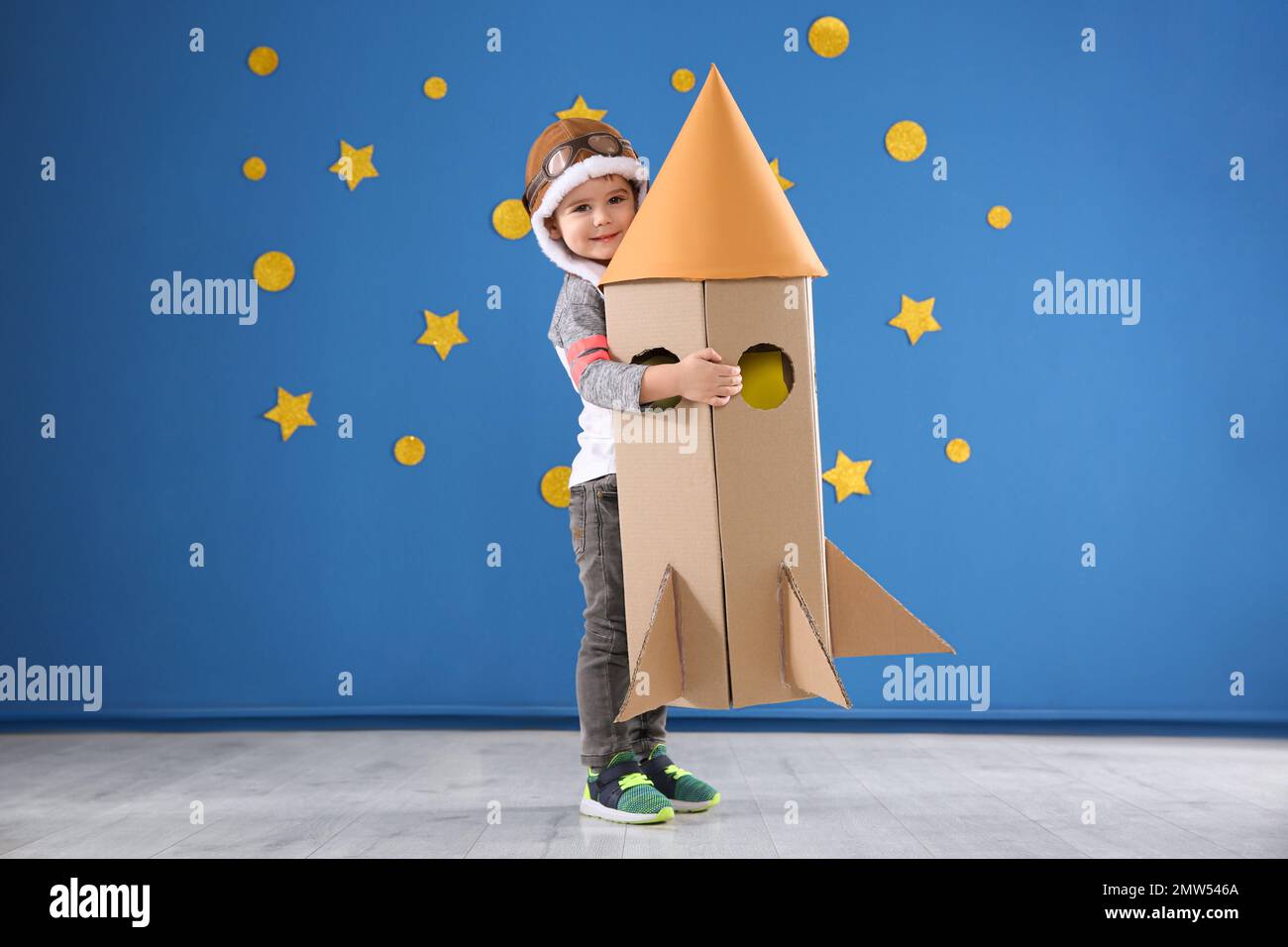 Cute little child playing with cardboard rocket near blue wall Stock ...