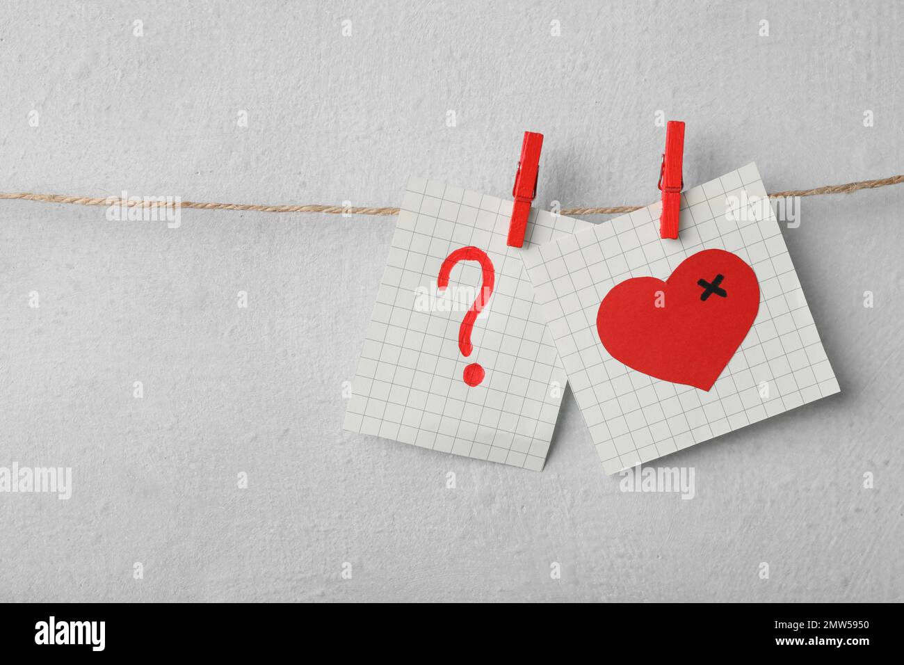 Paper notes with drawings of heart and question mark pinned on laundry string near light wall. Relationship problems concept Stock Photo