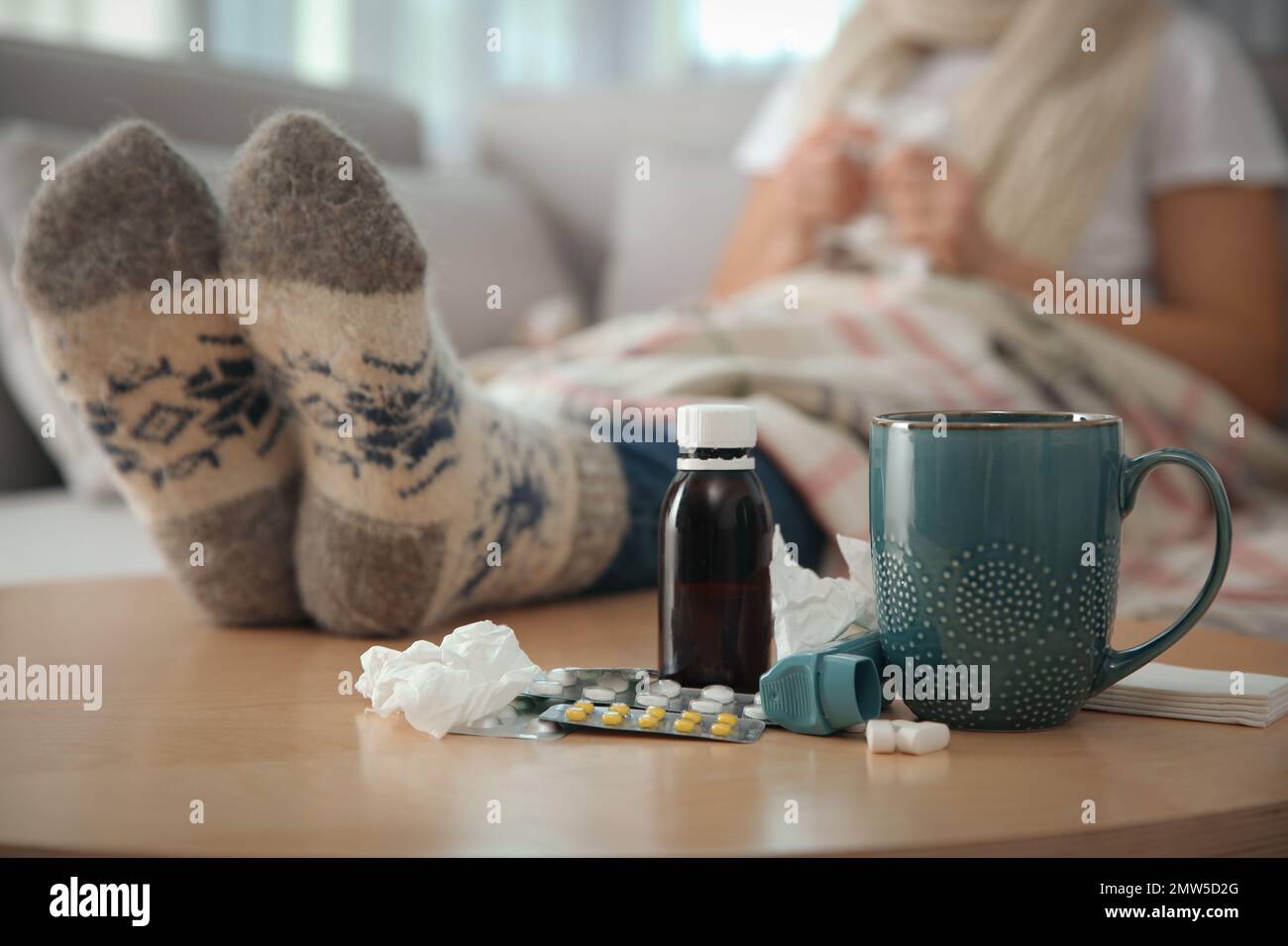 Person in warm socks near table with different remedies indoors, closeup. Influenza virus Stock Photo