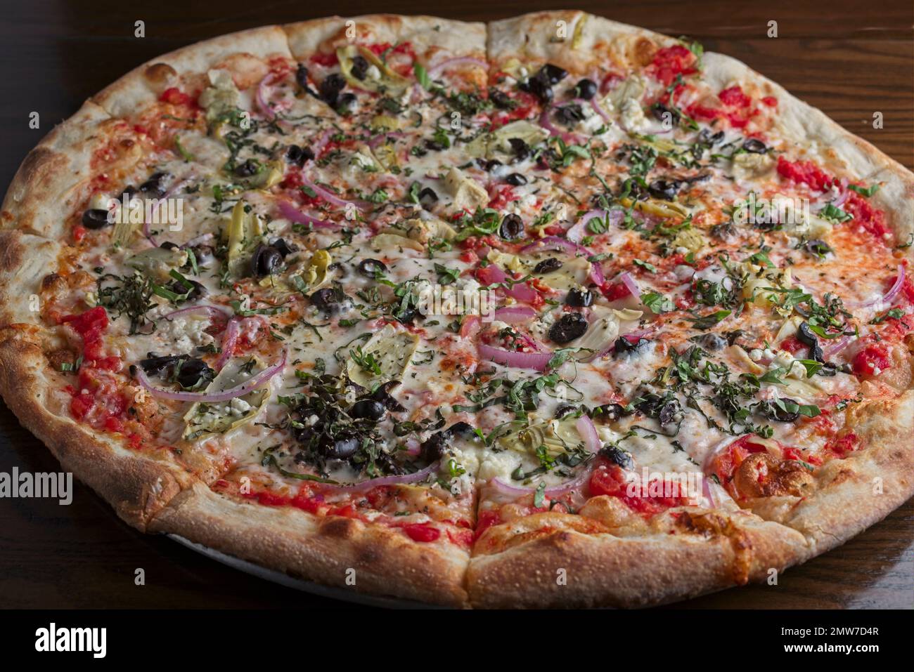 Gourmet pizza with fresh basil, feta cheese, artichoke, black olives