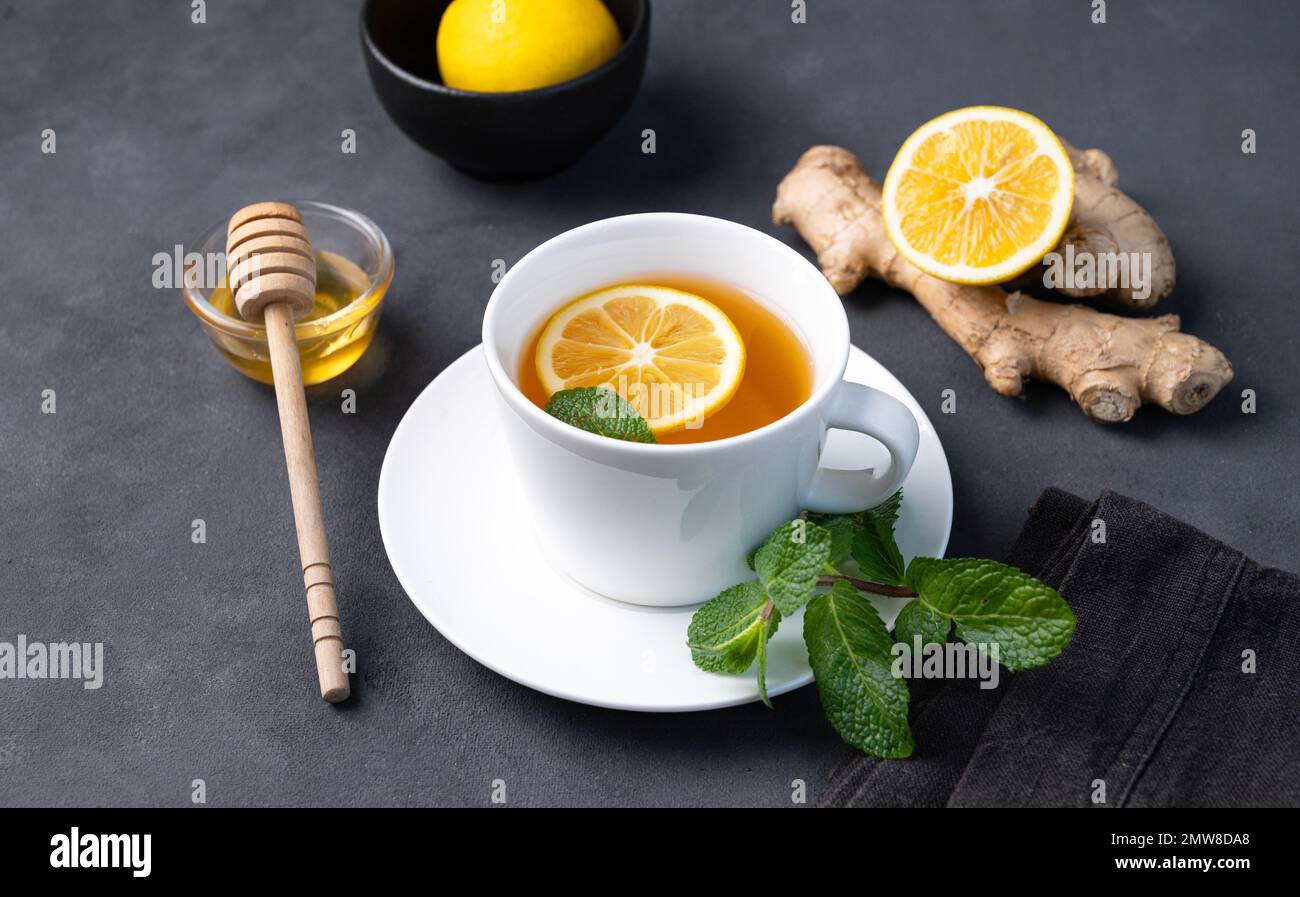 Cup of tea with lemon, honey and mint on a dark background. The concept of a healthy drink for immunity with ginger and herbs. Diet and antioxidant te Stock Photo