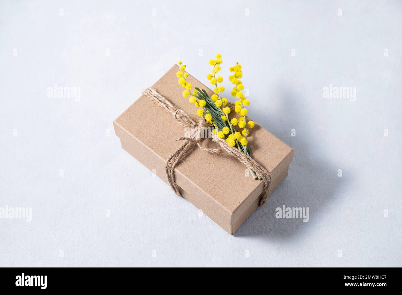 Gift craft box with yellow mimosa flowers on a light background. The concept for the spring holiday of women's Day or mother's day. Free space for tex Stock Photo