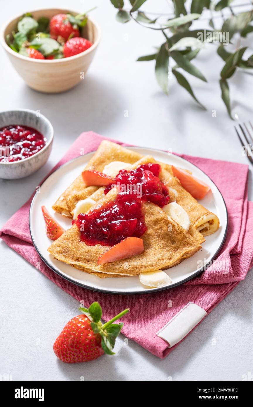 Sweet pancakes with berry jam, fresh strawberries and banana on a light background. The concept of homemade food. Top view. Stock Photo