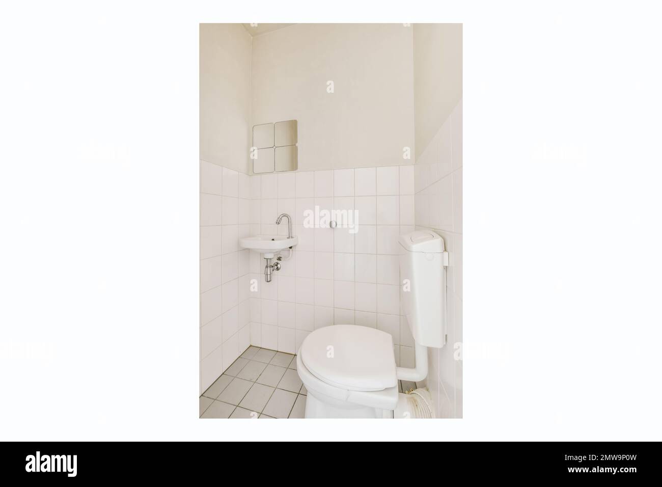 a white toilet in a small bathroom with tile flooring and wall - to - wall tiles on the walls Stock Photo