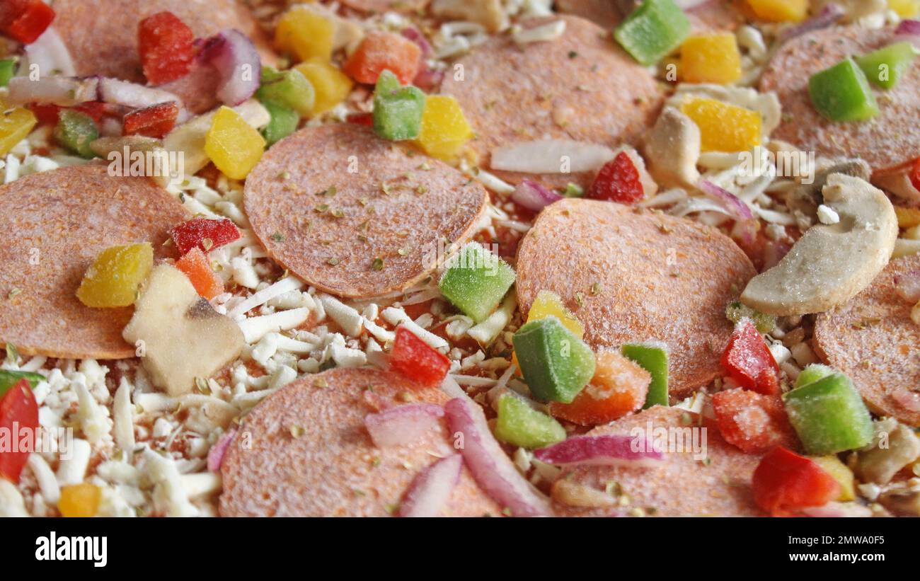 Frozen pizza before cooking. Toppings include pepperoni, diced red