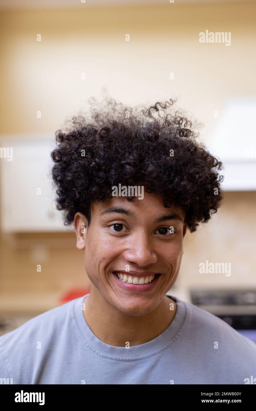 Vertical portrait of smiling biracial man with curly hair in kitchen at home Stock Photo