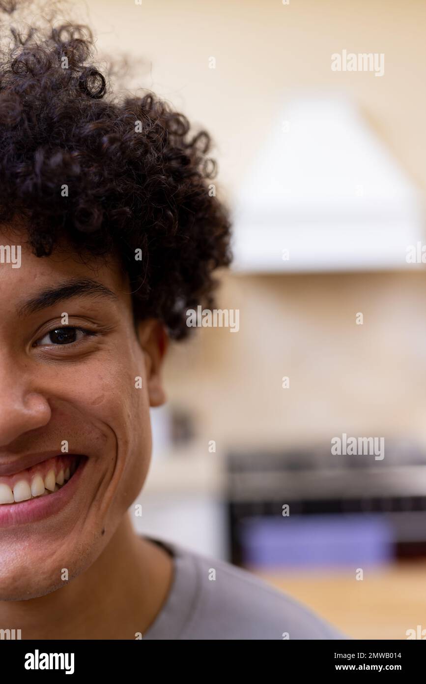 Vertical half face portrait of smiling biracial man with curly hair in kitchen at home, copy space Stock Photo