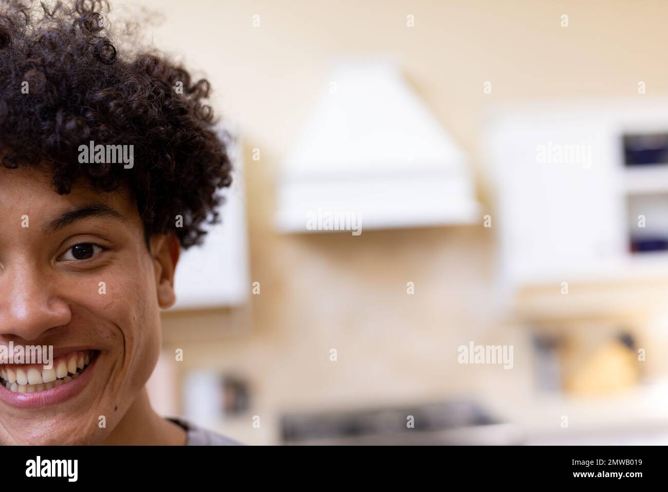 Half face portrait of smiling biracial man with curly hair in kitchen at home, copy space Stock Photo