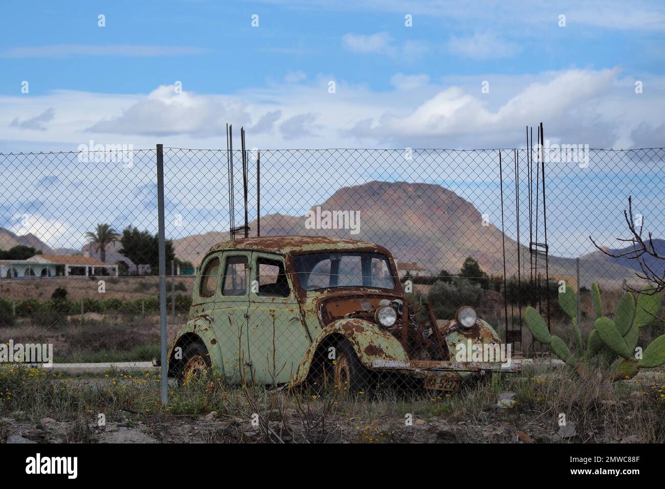 Rusty, demolished body of an old MG without bonnet behind fence made of wire mesh, Spain Stock Photo