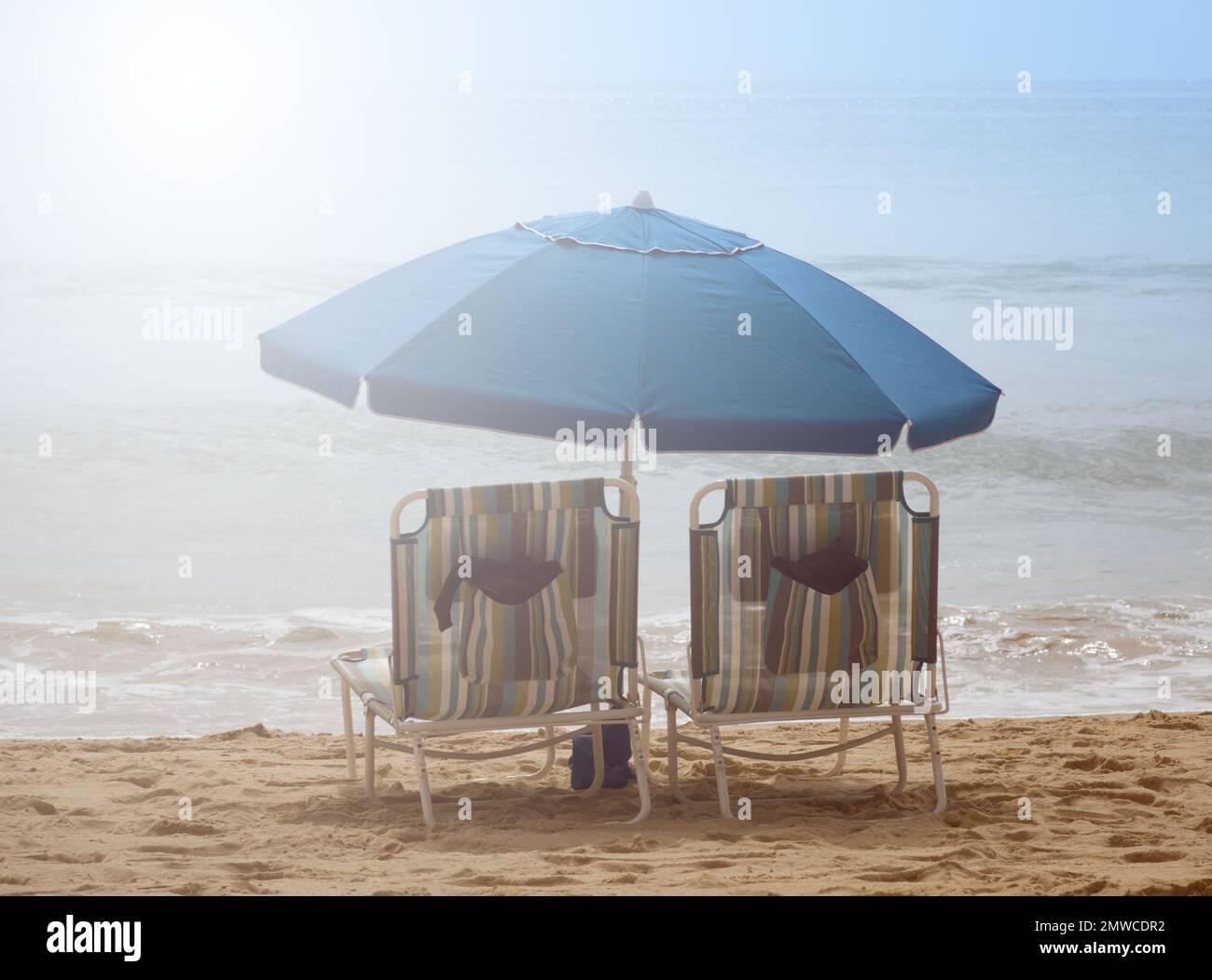 Two empty beach chairs with umbrellas on the Pacific Ocean during bright daylight Stock Photo