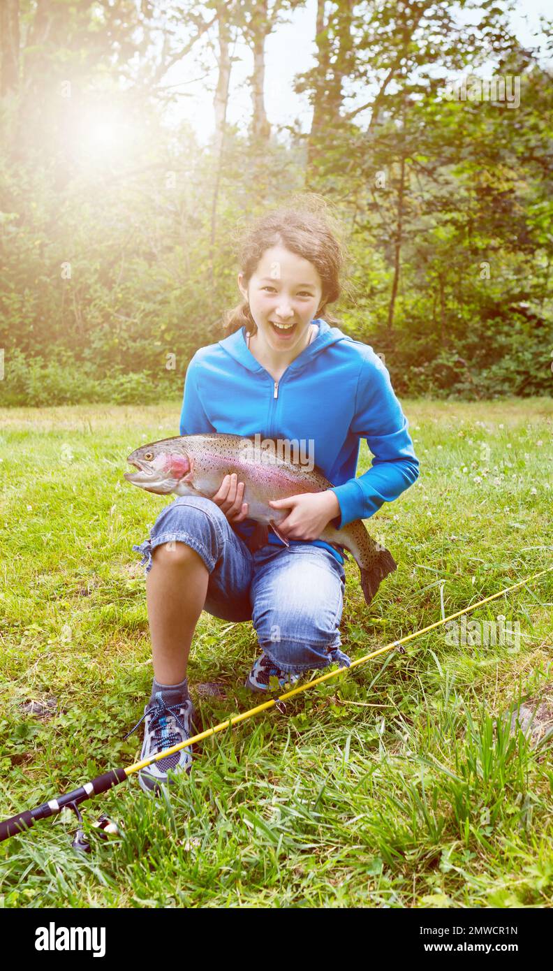 Young girl holding trout salmon which she caught on a bright summer day with lots of sunshine Stock Photo