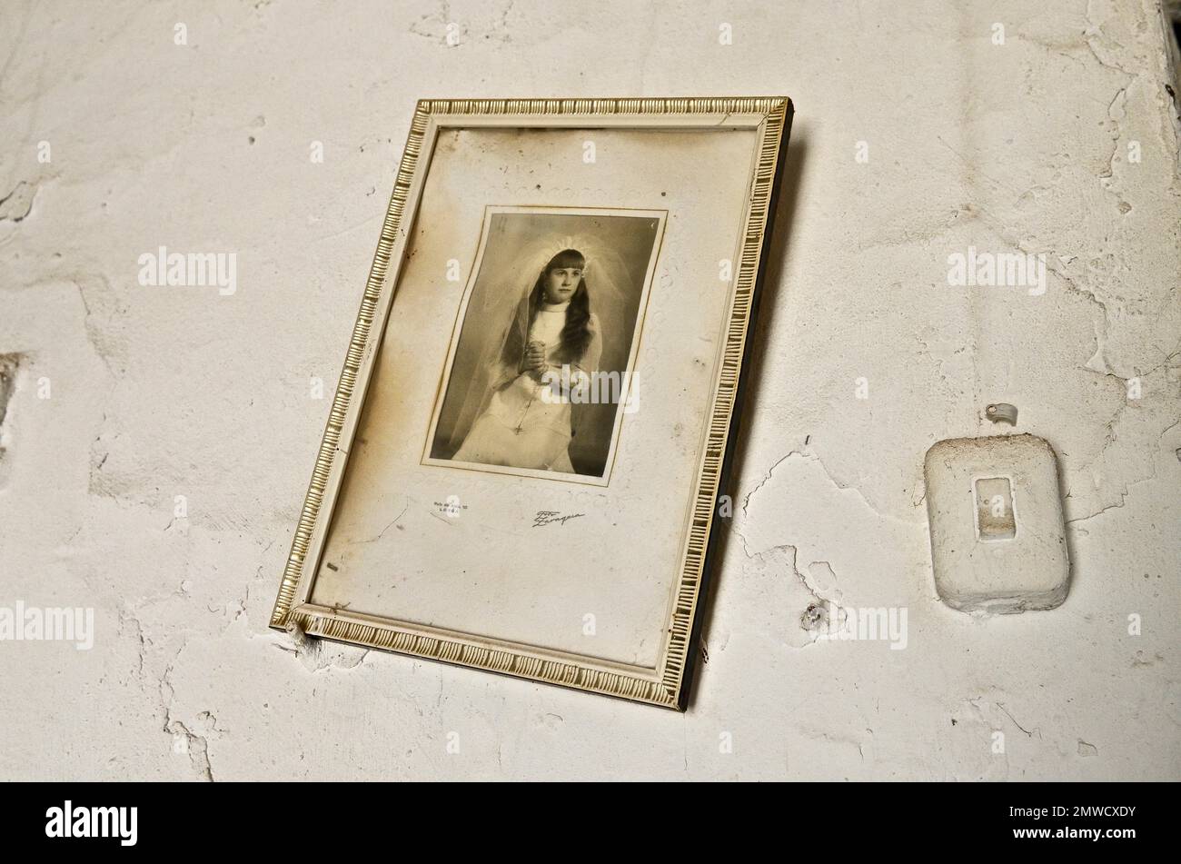 Framed photo on white wall of girl at communion, wall with picture and light switch, Spain Stock Photo