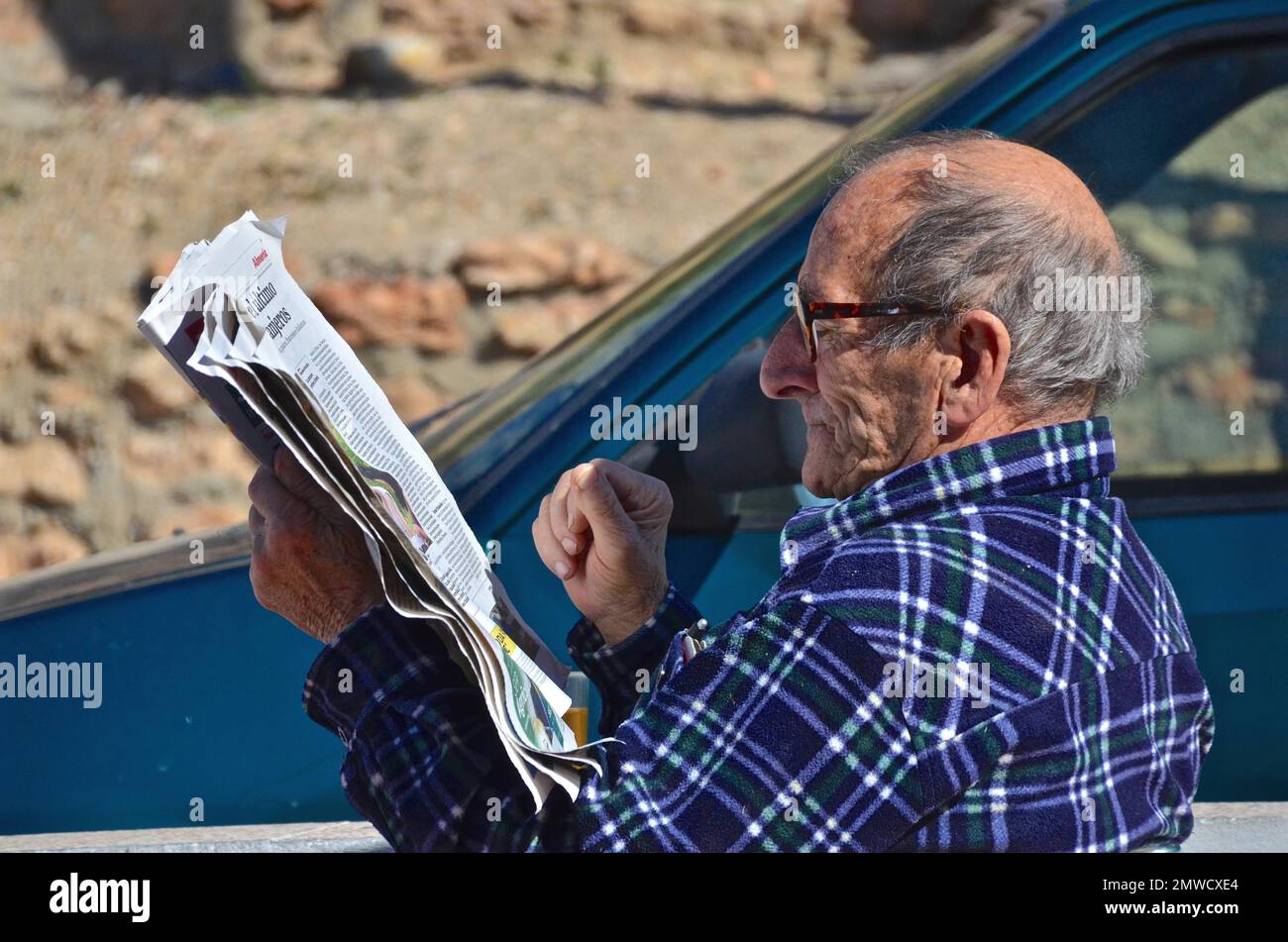 Old man with glasses reading newspaper in the street, Spain Stock Photo