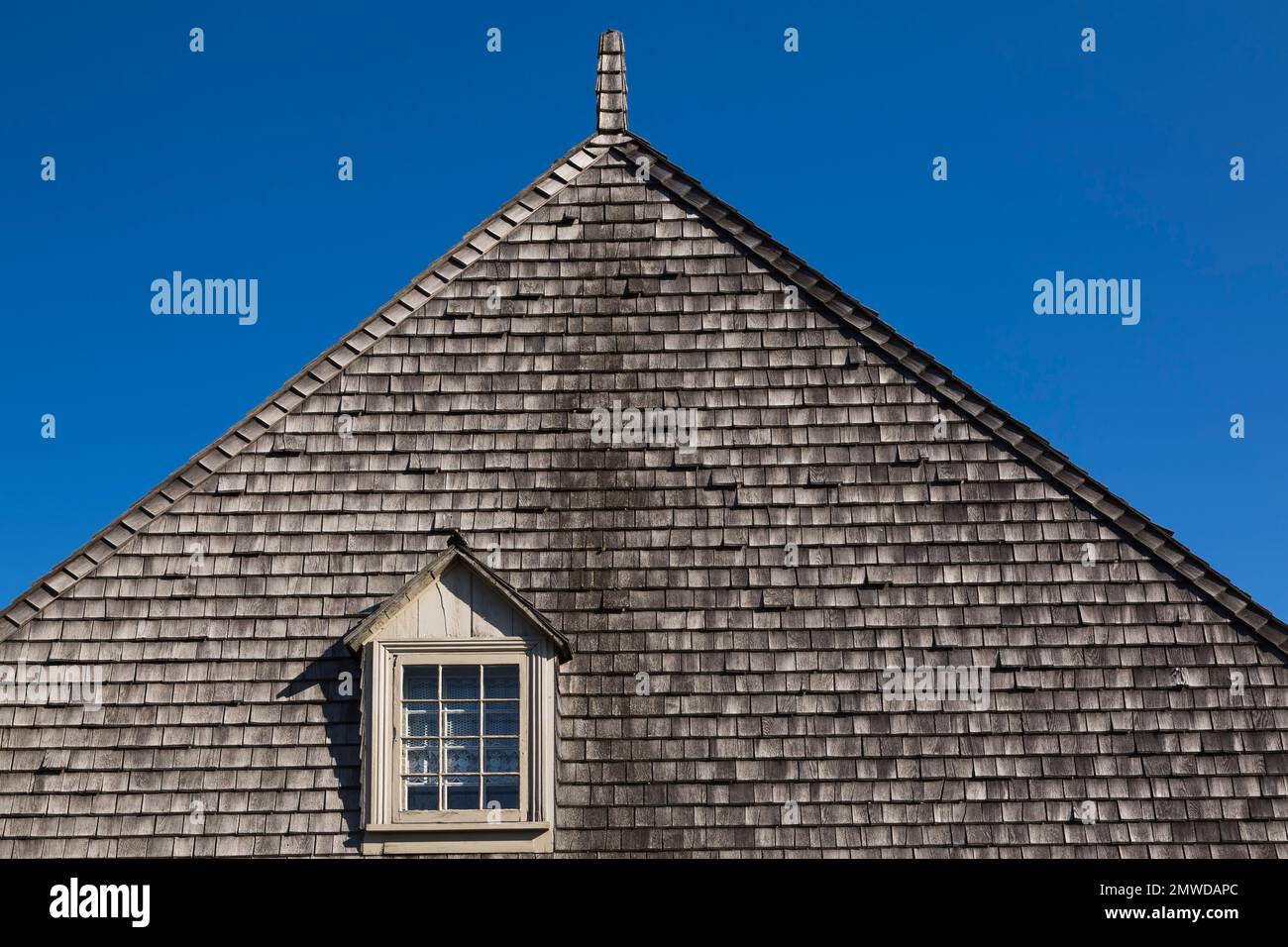 Closeup of tan coloured dormer window and cedar shingles roof on old