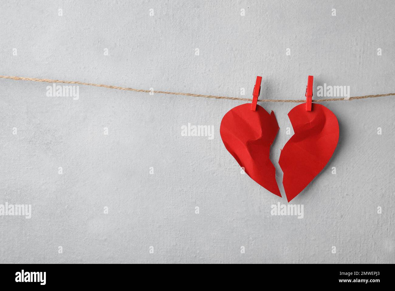 Halves of torn paper heart pinned on laundry string near light wall, space for text. Relationship problems concept Stock Photo