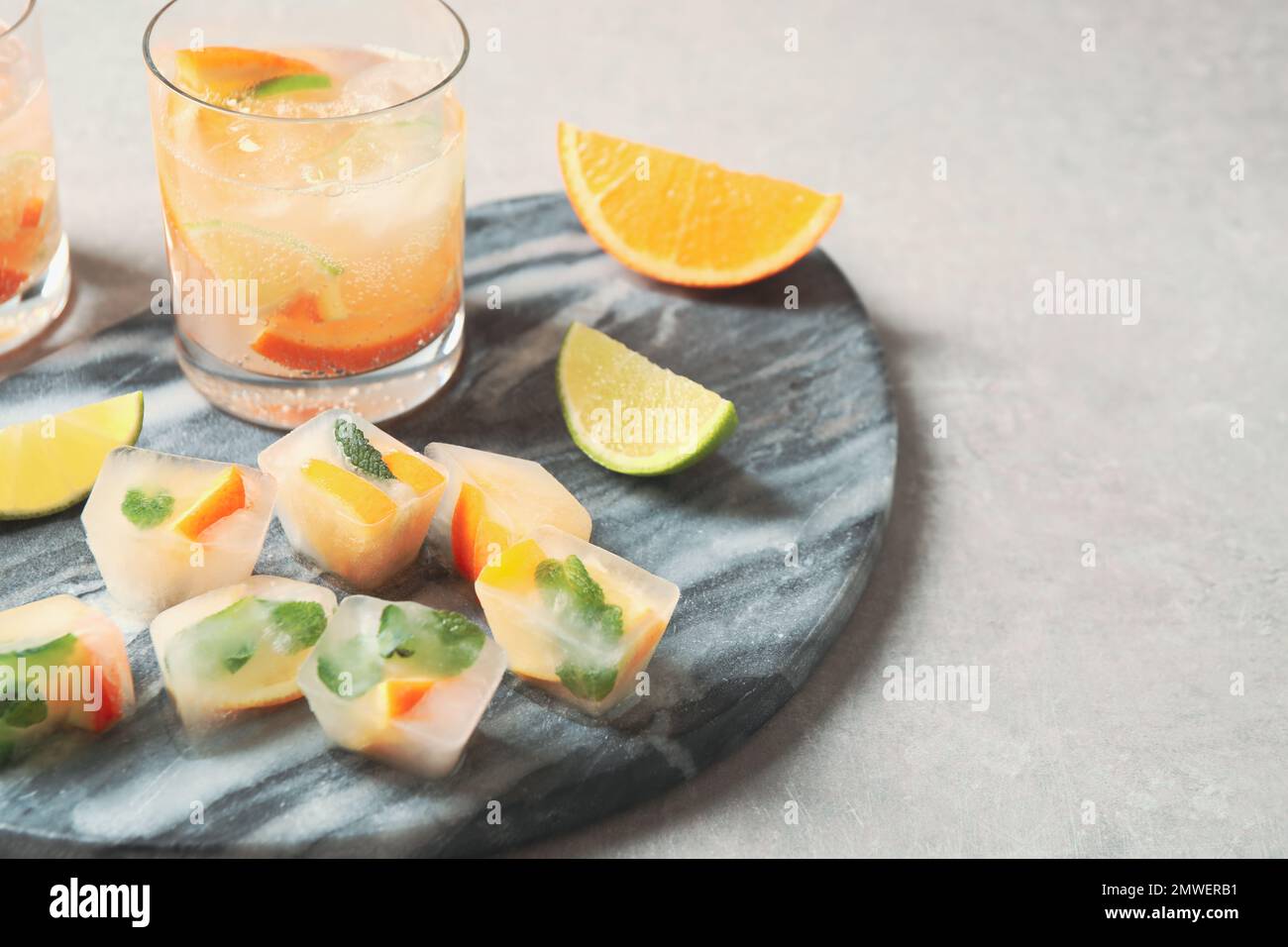 Ice cubes with orange and mint on light grey table Stock Photo