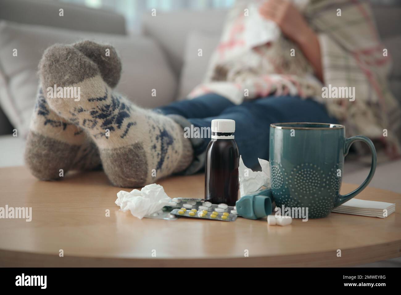 Person in warm socks near table with different remedies indoors, closeup. Influenza virus Stock Photo
