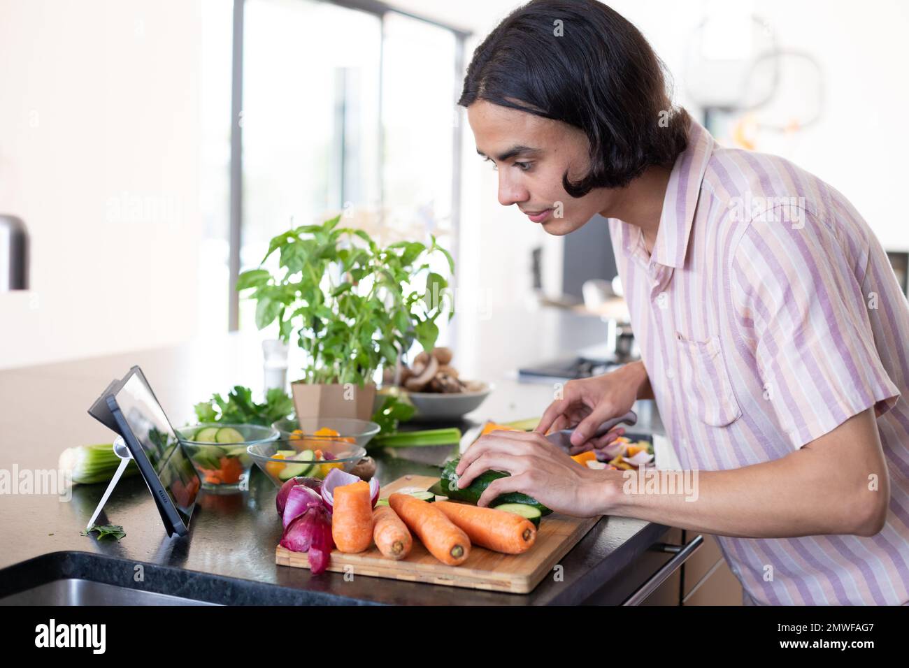 Happy biracial man cooking and using tablet in kitchen Stock Photo
