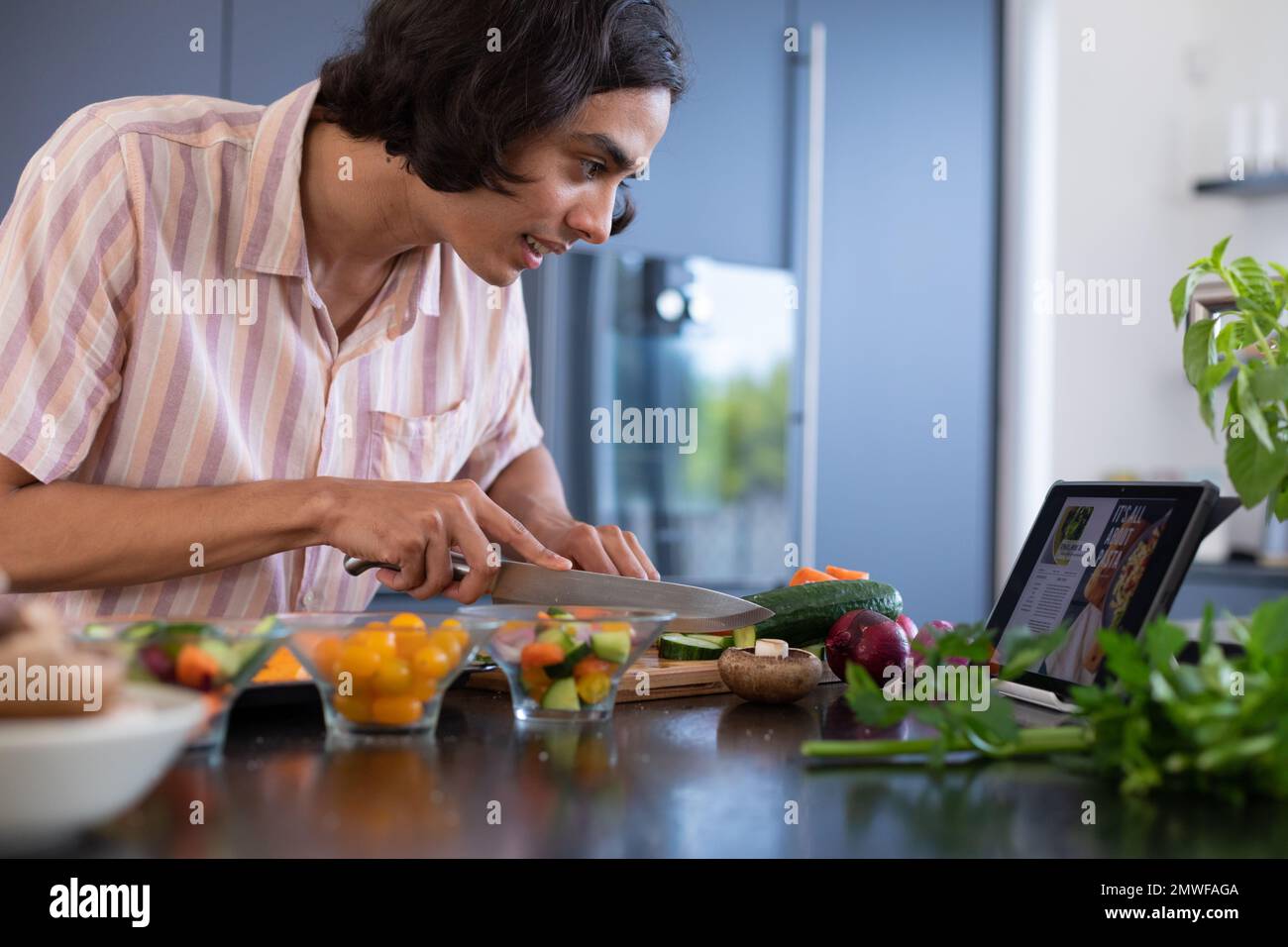 Happy biracial man cooking and using tablet in kitchen Stock Photo
