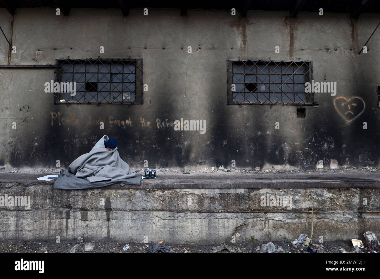 An Afghan refugee man wraps himself with a blanket to shield from the
