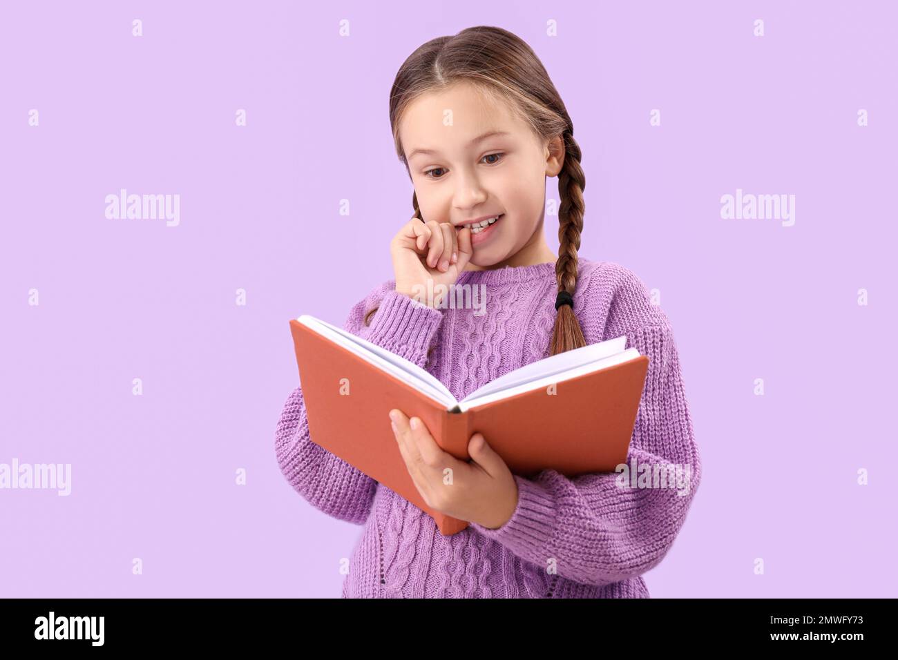 Little girl biting nails while reading book on lilac background Stock