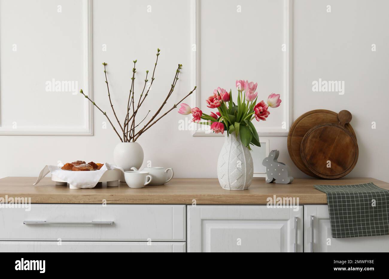 Vases with tulips, tree branches and Easter rabbit on counters in