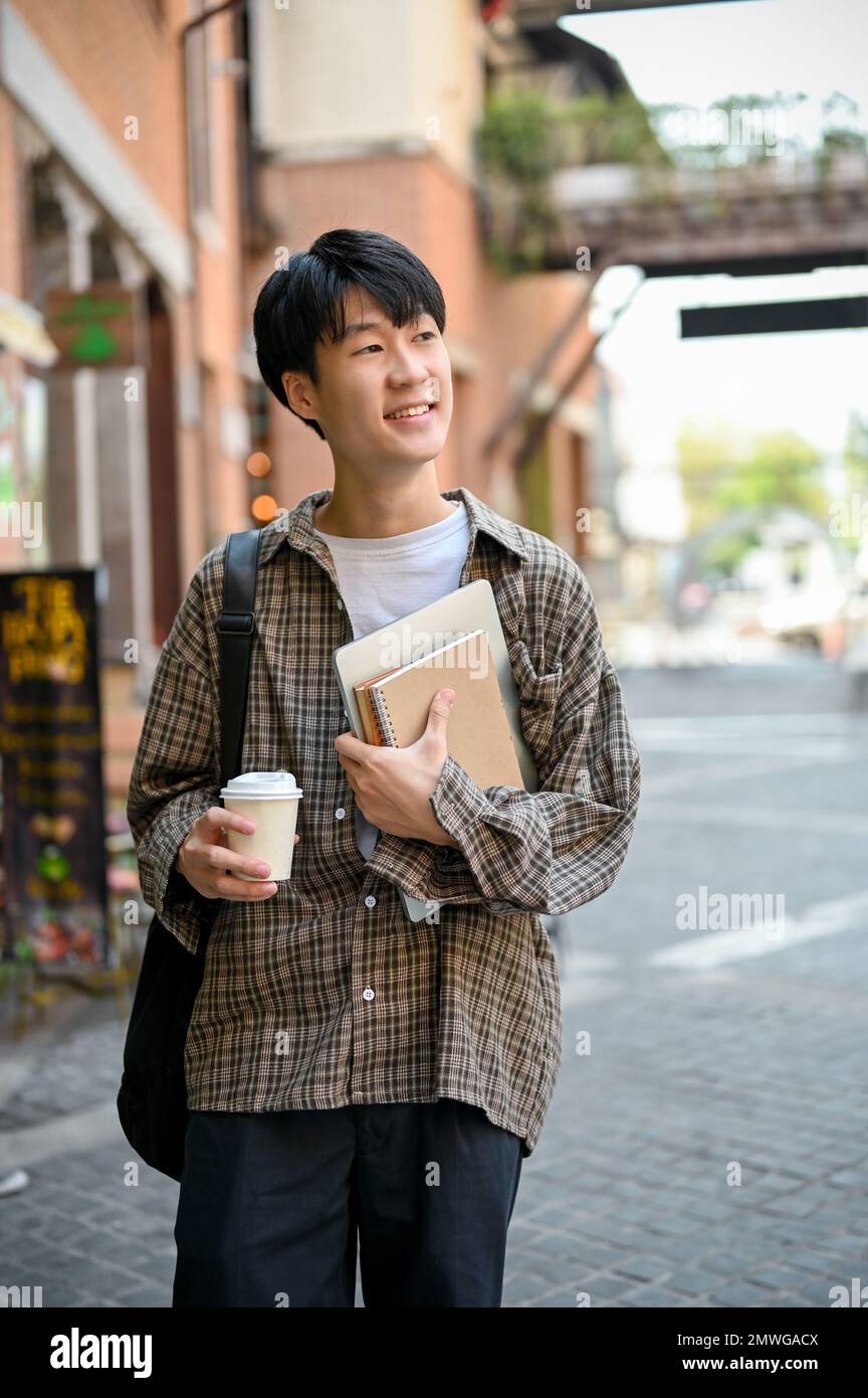Portrait of handsome and happy young Asian male college student in trendy  casual outfit with a coffee cup and his school book walking in the campus  or Stock Photo - Alamy