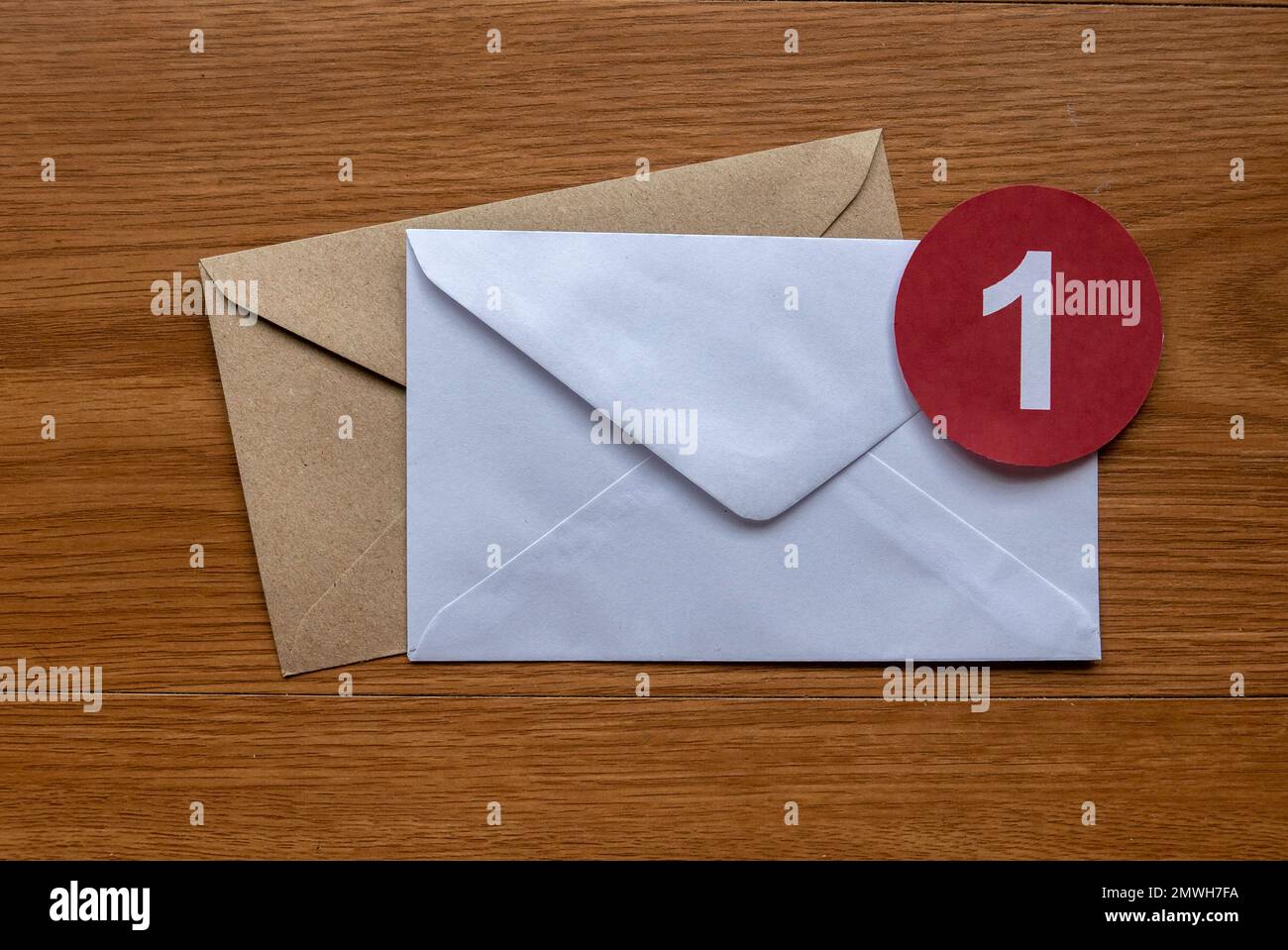 Concept of new email reminder or message alert. A white envelope with a red symbol of notification on a wooden background. Stock Photo