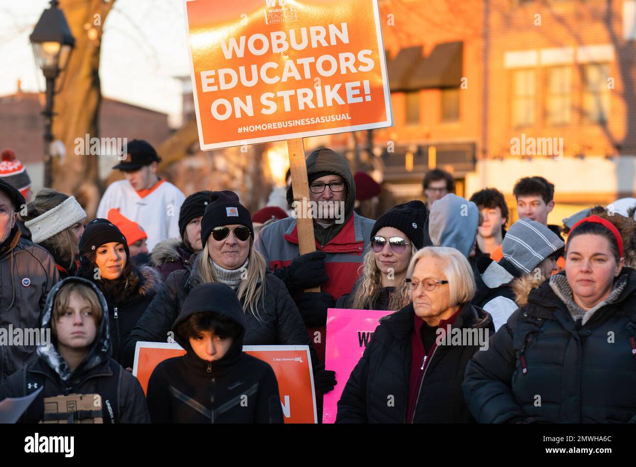 Educators listen to striking teachers and hold signs during a rally in