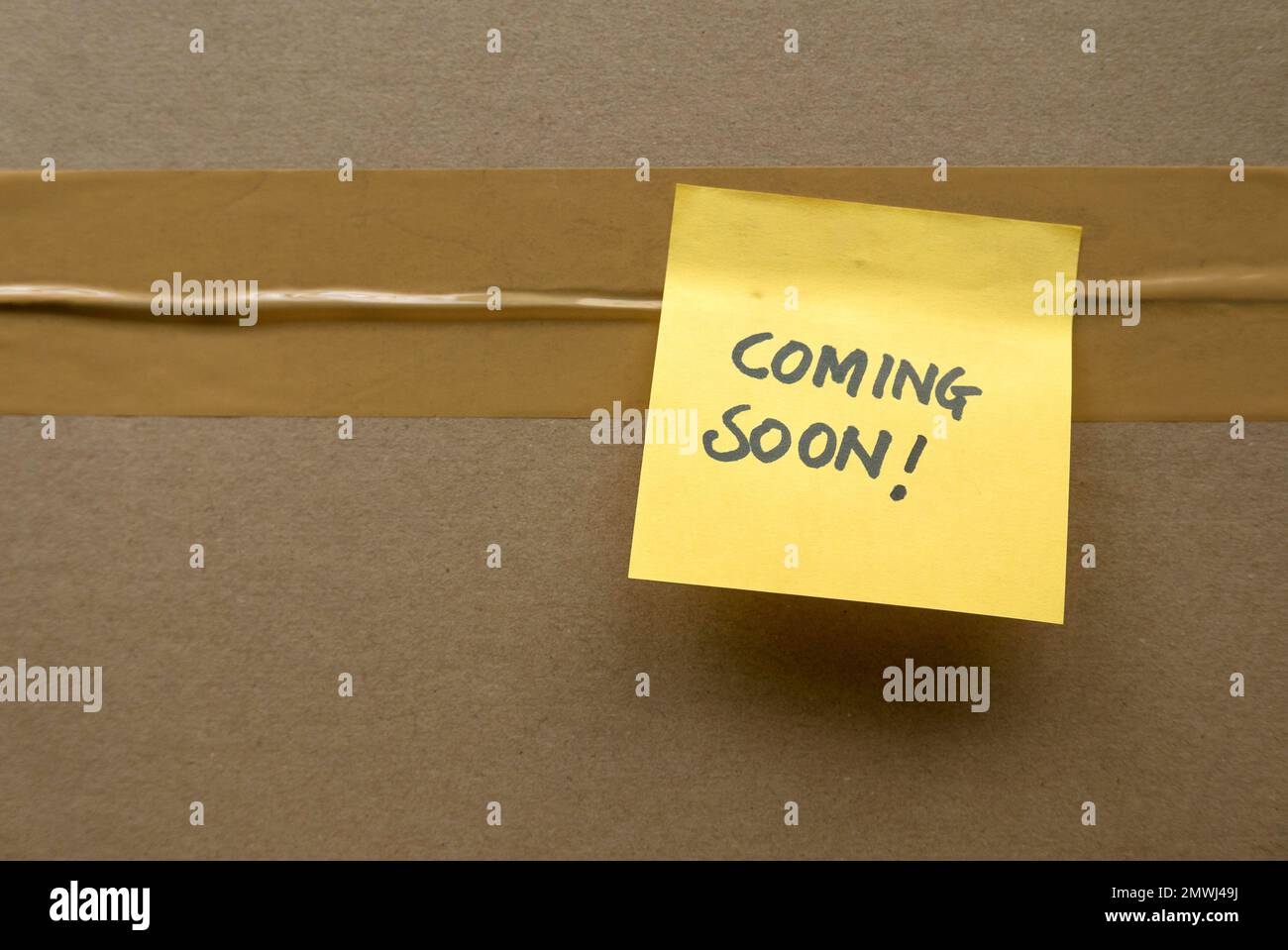 A box seal with adhesive tape and a yellow memo note written with coming soon. Stock Photo