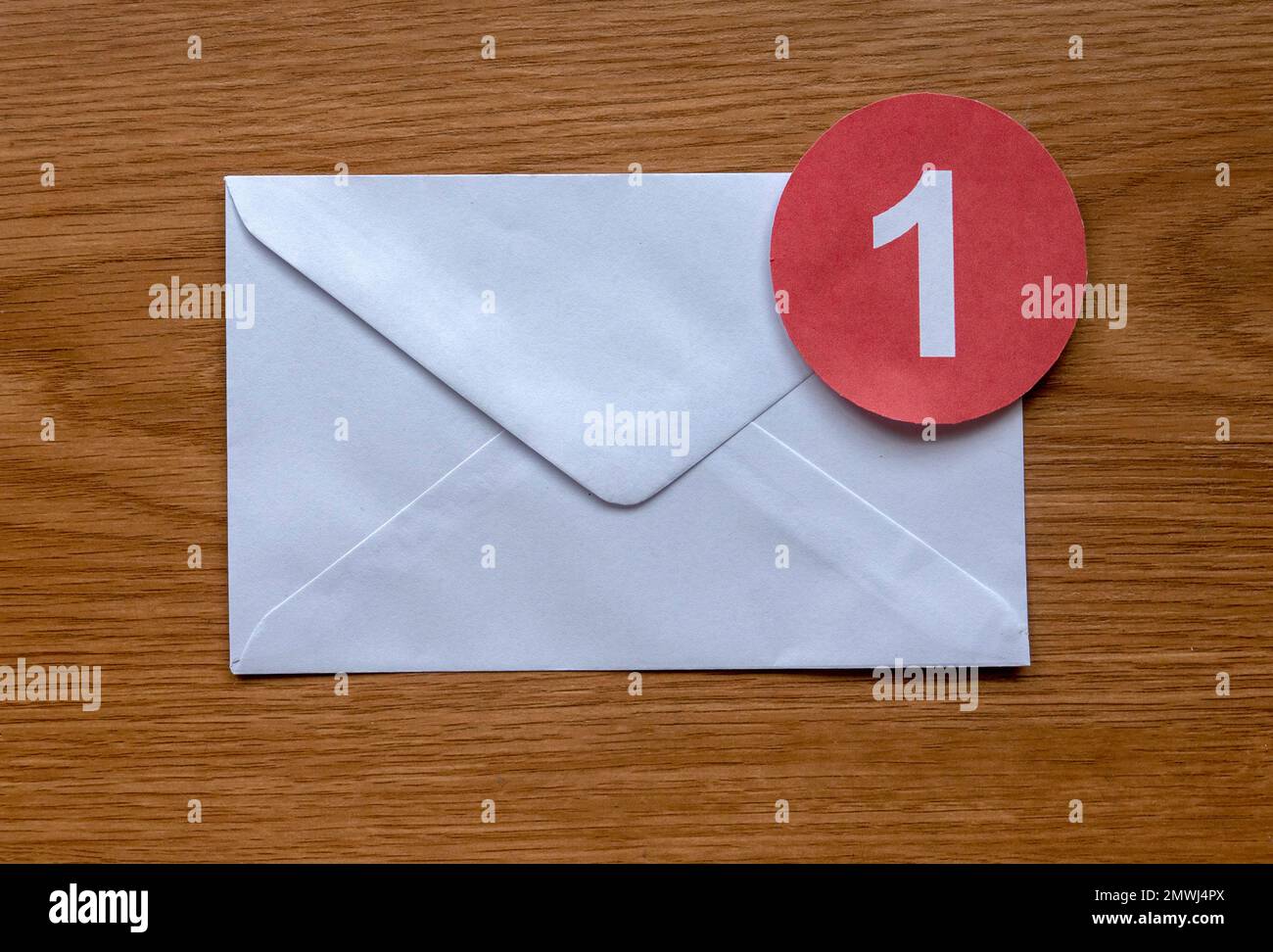 Concept of new email reminder or message alert. A white envelope with a red symbol of notification on a wooden background. Stock Photo