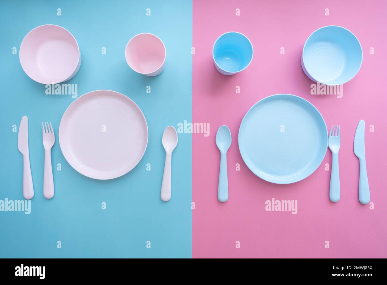 Flat lay baby feeding set. Sippy cup, plate, bowl, cutlery on pastel pink and blue background. Toddler self feeding training, baby weaning concept. Stock Photo