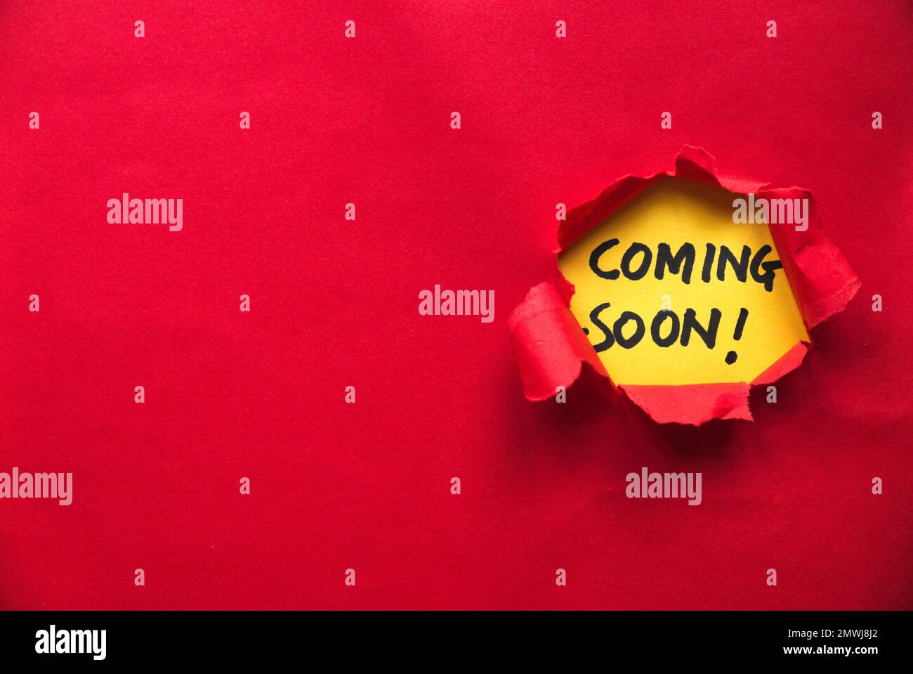 Red torn paper with a yellow paper written with coming soon. Copy space. Stock Photo