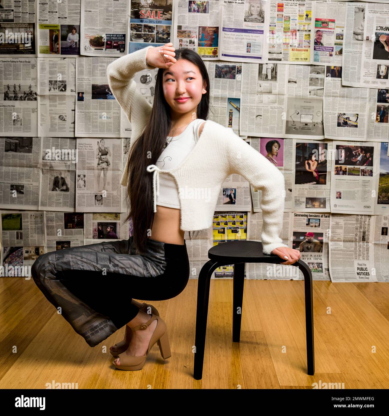 Full Body Tall Teenage Asian Girl Seated in Front of Backdrop of Newspapers Stock Photo