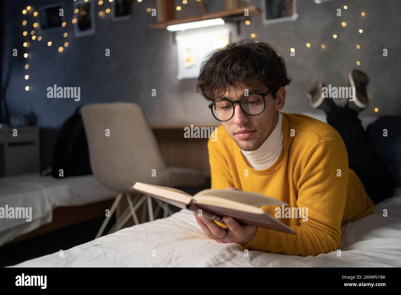 Leisure reading man is comfortable lying on her bed with a book, focused reading to prepare for a college exam. Copy space Stock Photo